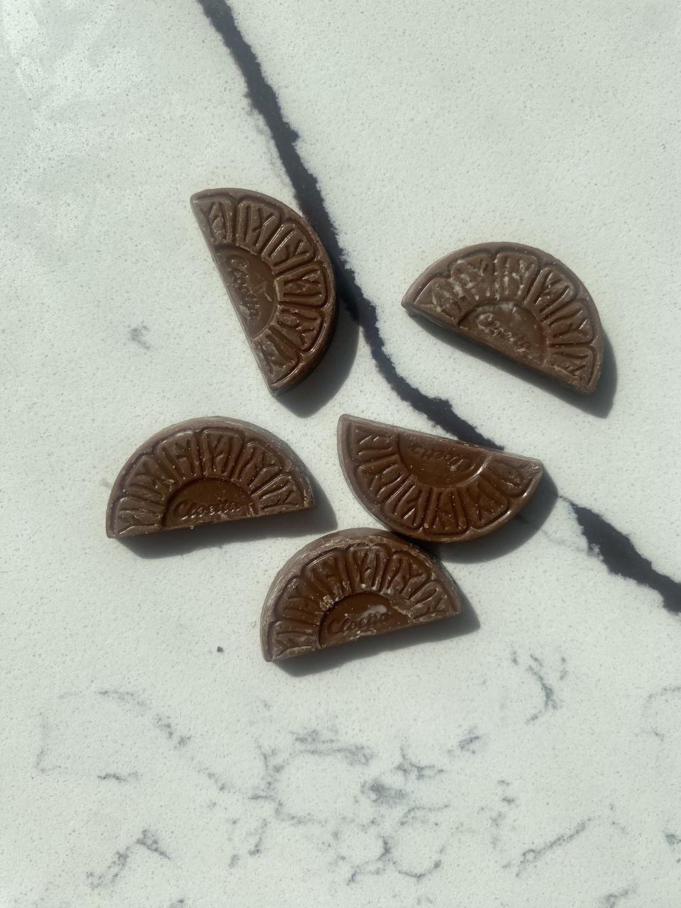 Five chocolate segments resembling citrus wedges are arranged on a marble surface