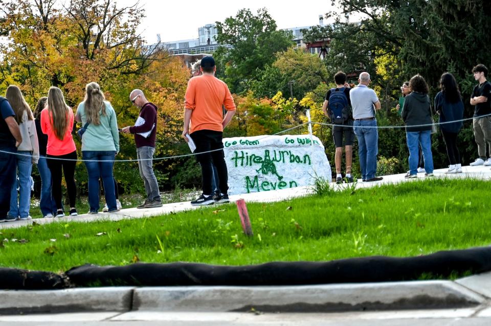 A prospective Michigan State University student tour stops at the Rock on Friday, Oct. 6, 2023, and views a message supporting the hiring of former Ohio State football coach Urban Meyer. "Go green, go white. Hire Urban Meyer," the text read on the East Lansing campus.