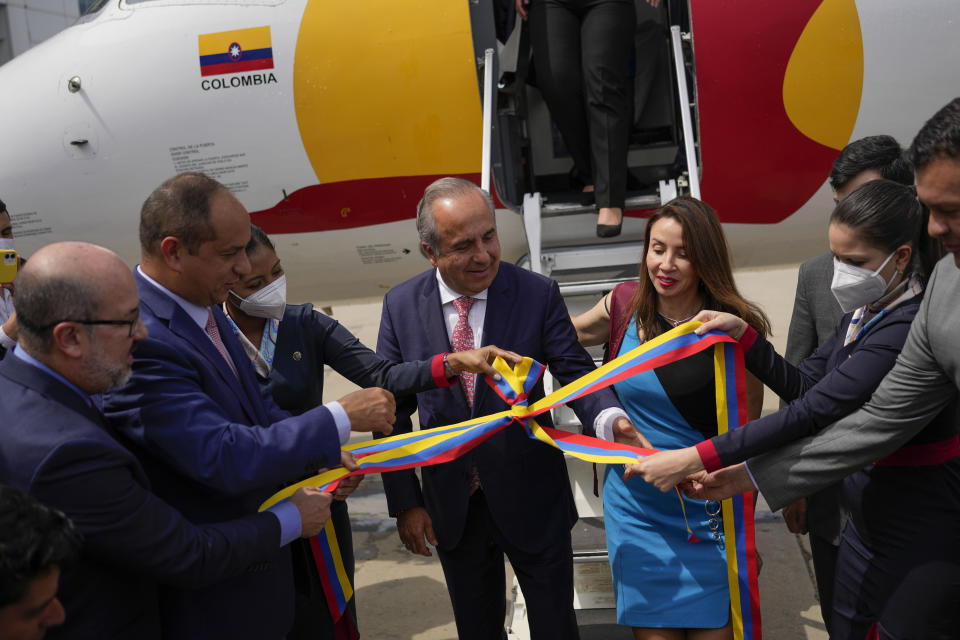 Guillermo Reyes, ministro de Transporte de Colombia, centro, y el ministro de Transporte de Venezuela, Ramón Velásquez, segundo desde la izquierda, desenrollan una cinta ceremonial después de que el avión de la aerolínea Satena que partió de Bogotá, Colombia, aterriza en el Aeropuerto Internacional Simón Bolívar en La Guaira, Venezuela, el miércoles 9 de noviembre de 2022. (AP Foto/Matías Delacroix)