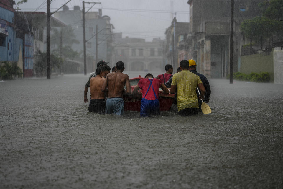 Residents push a boat through a flooded street to rescue a neighbor unable to leave his home on his own during a tropical cyclone in Havana, Cuba, Friday, June 3, 2022. Many of the island's people live along a coast prone to storms, hurricanes and the ravages of salty air and water, and now, the first rains of the new storm season have again exposed the fragility of Cuba’s housing. (AP Photo/Ramon Espinosa)