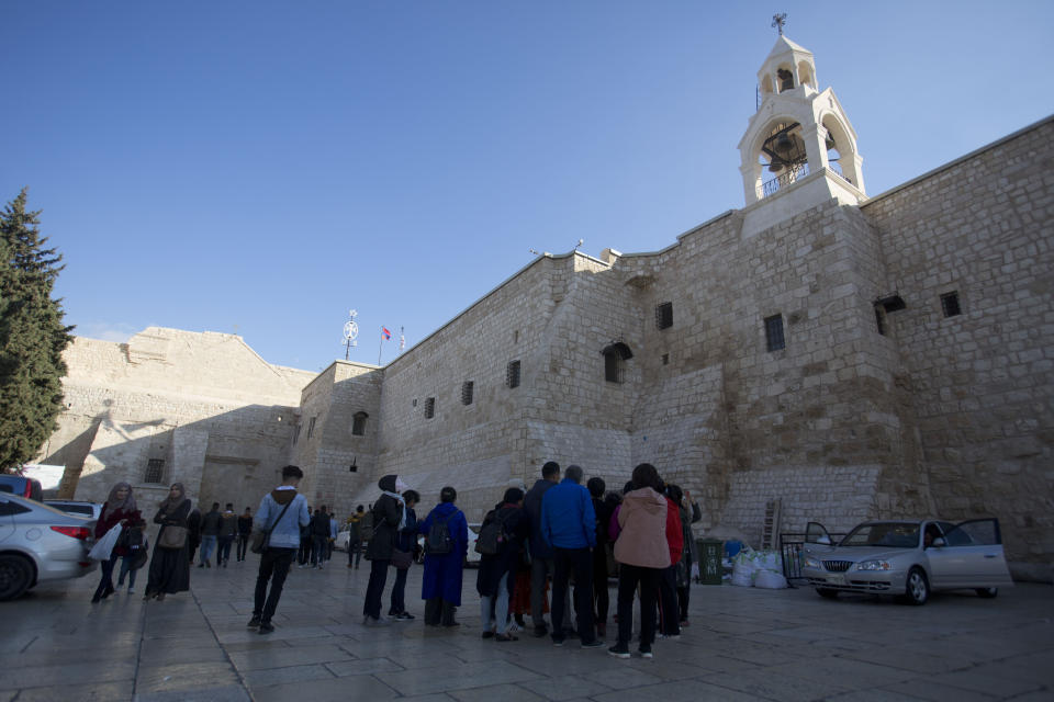 In this Thursday, Dec. 5, 2019 photo, Christian visitors gather outside the Church of the Nativity, traditionally believed by Christians to be the birthplace of Jesus Christ, in the West Bank city of Bethlehem. As visitors descend on Bethlehem this Christmas, they have the option of staying in restored centuries-old guesthouses, taking food tours of local markets, and perusing the dystopian art in and around a hotel designed by the British graffiti artist Banksy. (AP Photo/Majdi Mohammed)