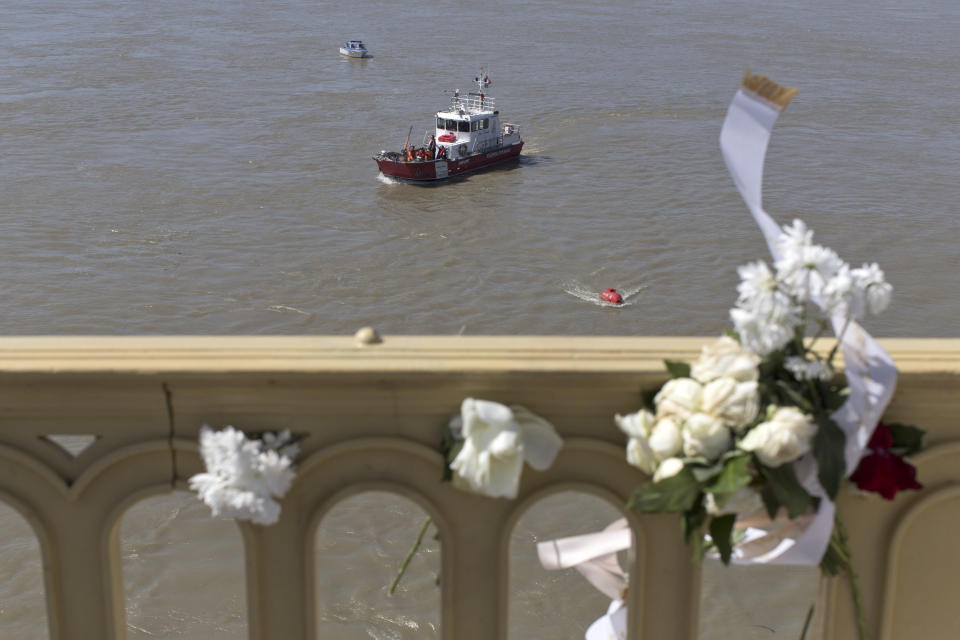 Flowers are seen on the railing of the Margit bridge as rescue boats work on the Danube river at the scene where a sightseeing boat capsized in Budapest, Hungary, Saturday, June 1, 2019. Rescue operations continue Saturday, and Hungarian authorities predicted it would take an extended search to find the 21 people still missing after a boat carrying South Korean tourists was rammed Wednesday night by a cruise ship and sank. (AP Photo/Marko Drobnjakovic)