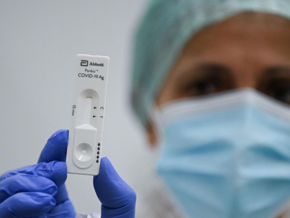 Women with mask, hat and gloves holds up rapid test.