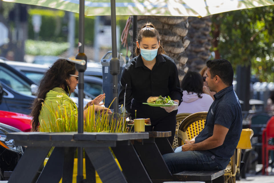 Redondo Beach, CA - May 14:A masked server delivers food to customers along S. Catalina Avenue in the Riviera Village shopping area of Redondo Beach, CA, a day after the Centers for Disease Control and Prevention (CDC) loosened guidelines for vaccinated people, with masks no longer being necessary when outdoors or in most indoor situations, Friday, May 14, 2021. The new guidelines state that fully vaccinated people no longer need to wear a mask or physically distance in any setting, except where required by federal, state, local, tribal, or territorial laws, rules, and regulations, including local business and workplace guidance. (Jay L. Clendenin / Los Angeles Times via Getty Images)