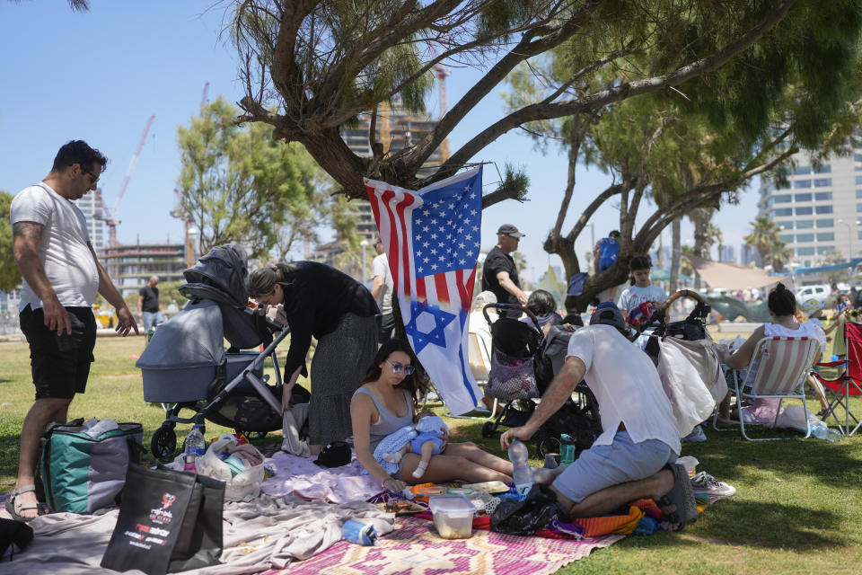 A woman holds her baby as she sits next to a flag displaying Israeli and U.S. national symbols together during Israel's Independence Day celebrations in Tel Aviv, Tuesday, May 14, 2024. Israelis are marking 76 years since Israel's creation. (AP Photo/Ohad Zwigenberg).