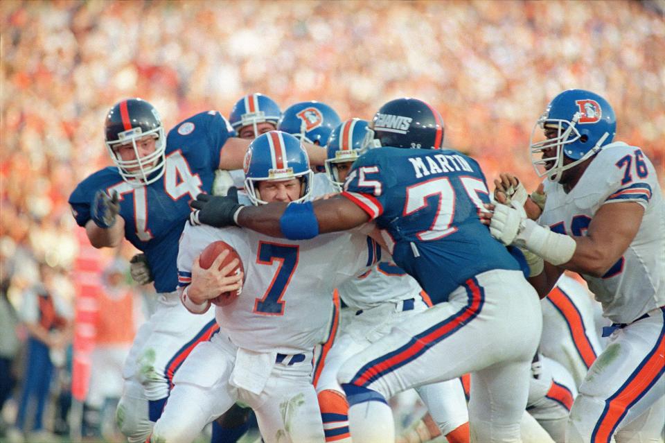 FILE - Denver Broncos quarterback John Elway gets sacked for a safety by New York Giants left end George Martin (75) in the second quarter of Super Bowl XXI, Jan. 25, 1987 in Pasadena, Calif. (AP Photo/Lennox Mclendon, File)