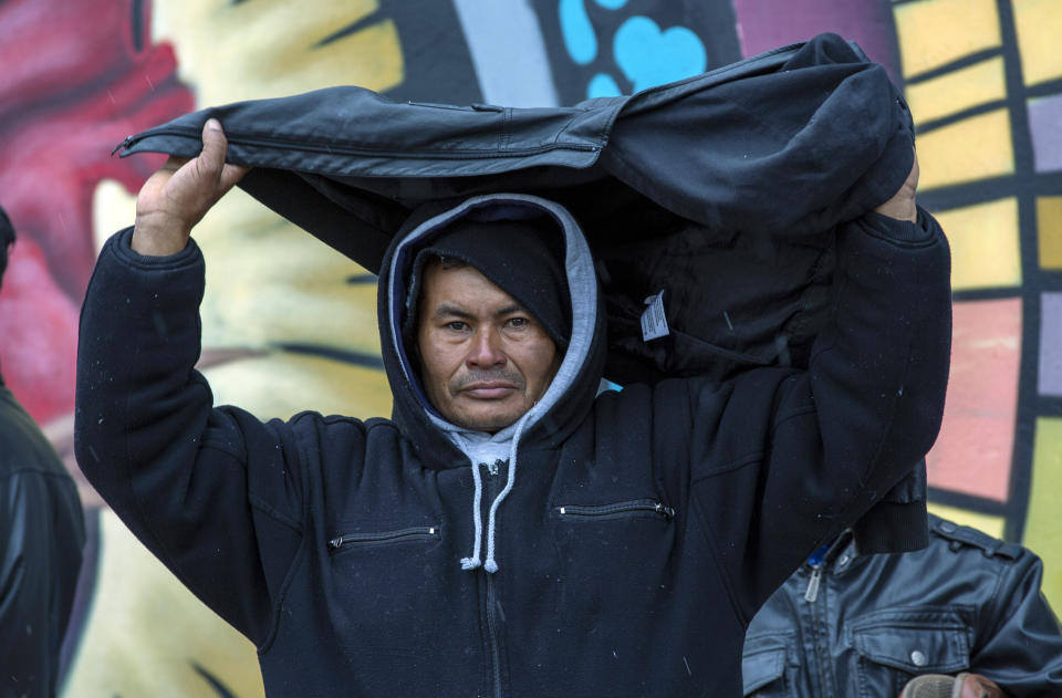 A migrant from El Salvador covers himself from a light winter drizzle while camping on a street in downtown El Paso, Texas, Sunday, Dec. 18, 2022. Texas border cities were preparing Sunday for a surge of as many as 5,000 new migrants a day across the U.S.-Mexico border as pandemic-era immigration restrictions expire this week, setting in motion plans for providing emergency housing, food and other essentials. (AP Photo/Andres Leighton)