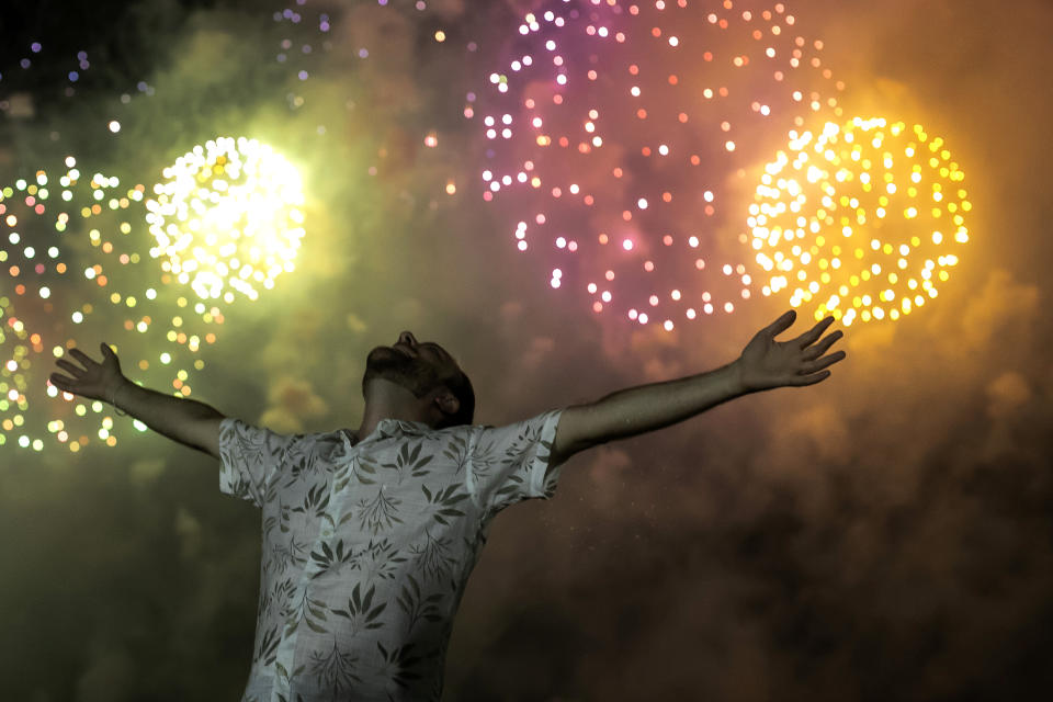 A man celebrates the start of the New Year, backdropped by fireworks exploding in the background over Copacabana Beach in Rio de Janeiro, Brazil, Saturday, Jan. 1, 2022. (AP Photo/Bruna Prado)