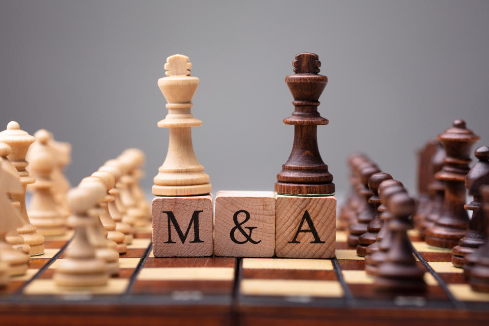 The black and white kings in the middle of a chess board standing on top of block letters that spell out "M&A".