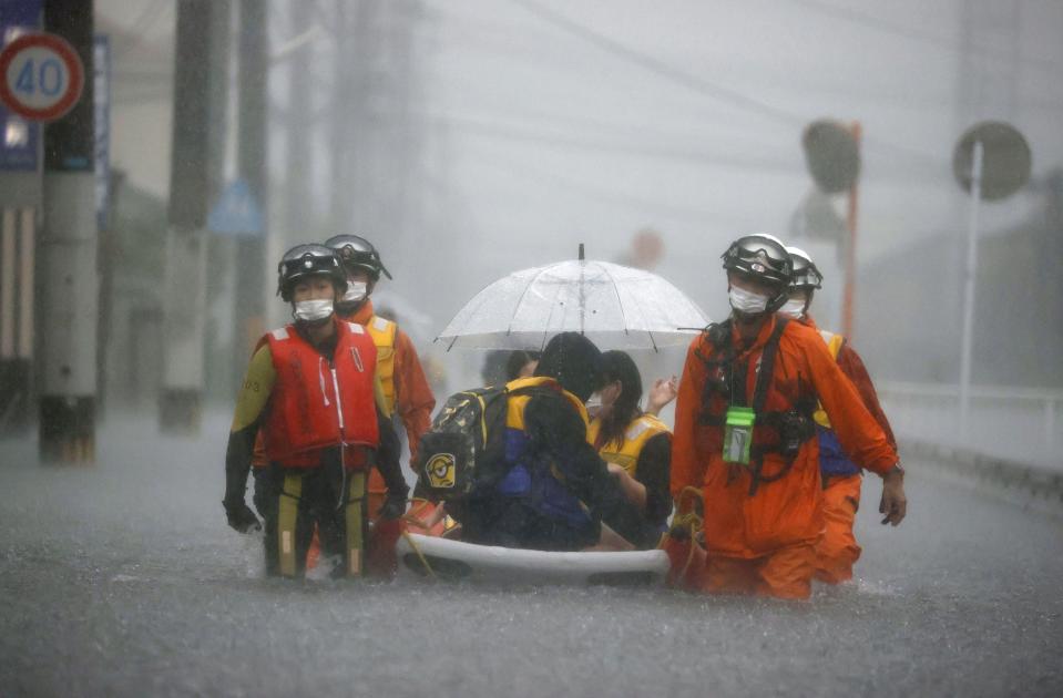 FILE - Firefighters carry stranded residents on boat in a road flooded by heavy rain in Kurume, Fukuoka prefecture, western Japan, Aug. 14, 2021. As fossil fuel use that feeds climate change is creeping up around the world, Japan is set for another sweltering summer following last year’s dangerous heat waves and is at growing risk of flooding and landslides. (Kyodo News via AP, File)