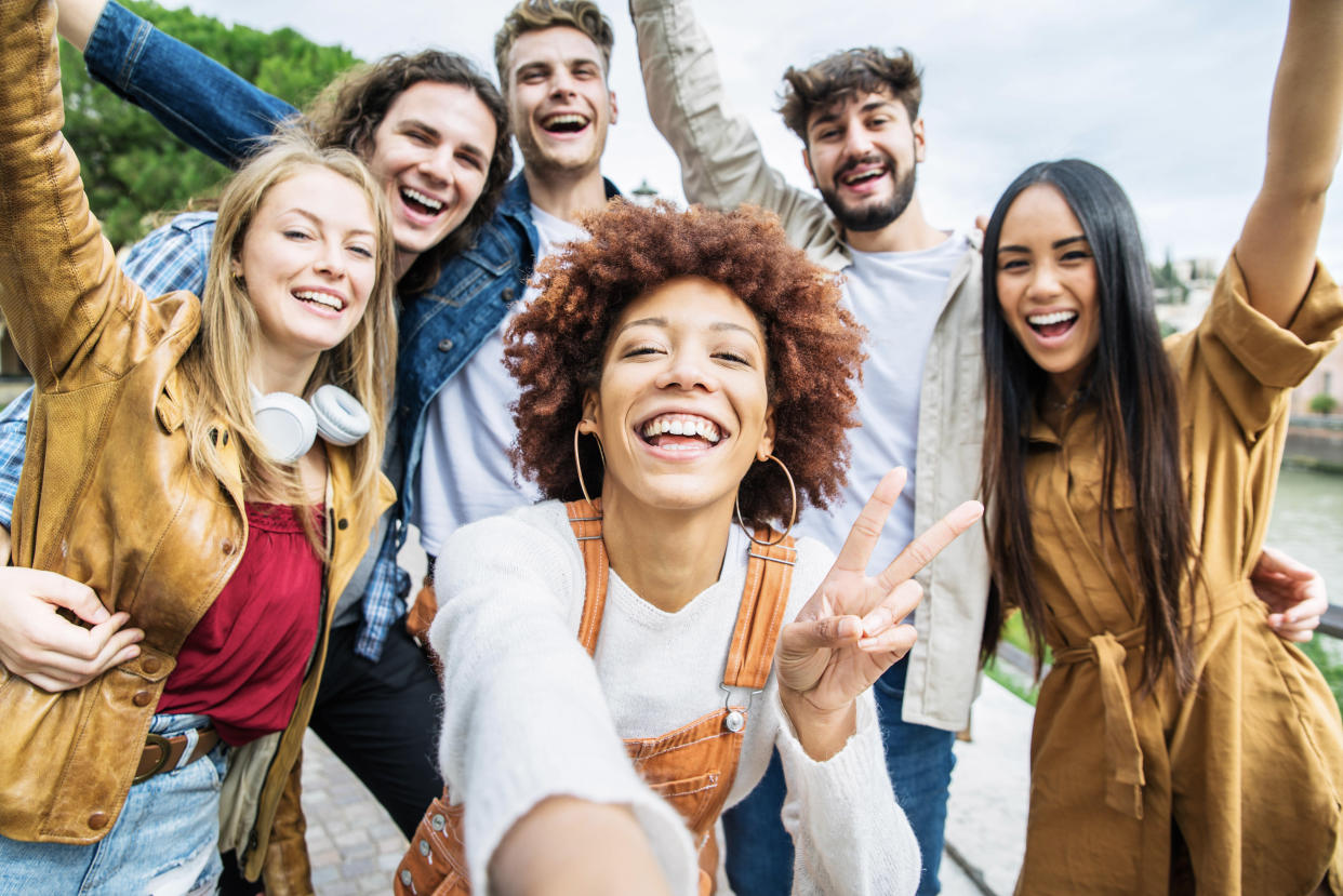 Six friends smile and wave for a photo. 