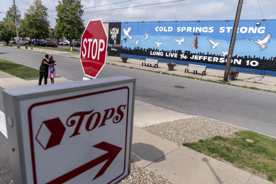 On Monday, Aug. 21, 2023, two people embrace outside a mural memorializing the 10 people killed when a shooter targeted Black shoppers at a Tops supermarket in 2022, in Buffalo, N.Y. (AP Photo/David Goldman)