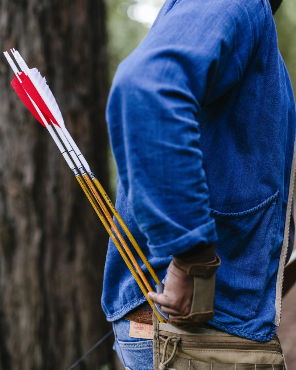 A person wearing a blue shirt reaches into a quiver of arrows.