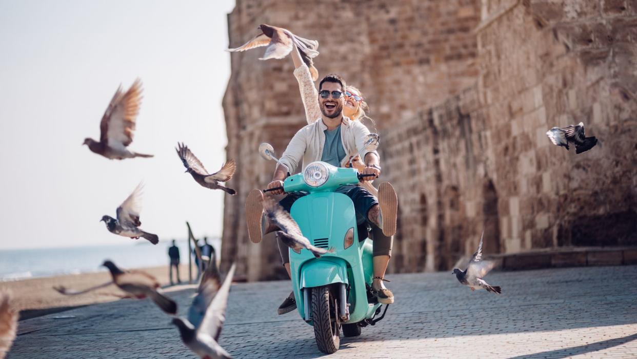 Tourist friends on summer holidays in Europe having fun riding retro scooter by the sea.