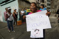 A woman with toothpaste under her nose to help with the effects of tear gas fired by security forces holds a sign that reads in Spanish "Get out Maduro," referring to Venezuelan President Nicolas Maduro, in the Cotiza neighborhood of Caracas, Venezuela, Monday, Jan. 21, 2019. Security forces have fired tear gas against protesters in a poor neighborhood near the presidential palace after an apparent uprising by a national guard unit. (AP Photo/Ariana Cubillos)