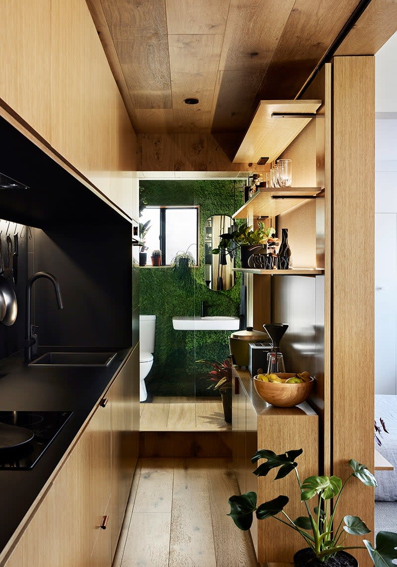 A narrow bathroom with bamboo flooring, walls, and ceiling; a black bathroom sink area; and a living wall at the far end behind the toilet.