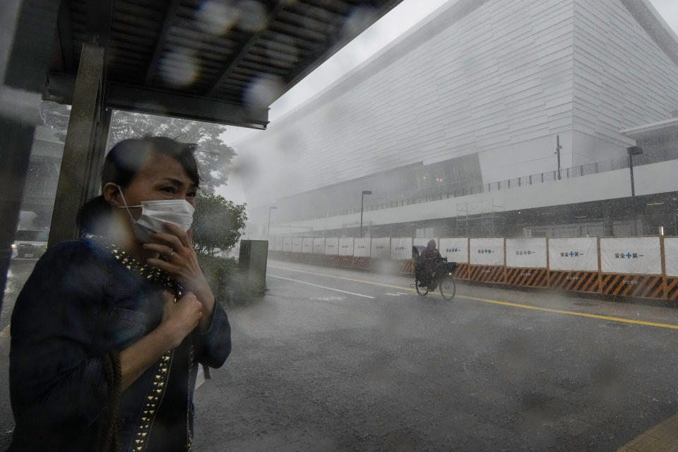 A woman takes shelter under a bus stop as heavy rain and hail come down outside Ariake Arena, where Olympic volleyball will be held, Sunday, July 11, 2021, in Tokyo. The fourth state of emergency would go in effect on Monday and last through Aug. 22, despite the opening ceremony of Tokyo Olympics that's scheduled to be held in less than two weeks. (AP Photo/Kiichiro Sato)