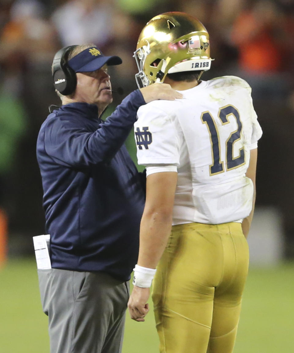 Notre Dame head coach Brian Kelly, left, talks with quarterback Tyler Buchner (12) during the second half of an NCAA college football game against Virginia Tech in Blacksburg, Va., Saturday, Oct. 9, 2021. (AP Photo/Matt Gentry)