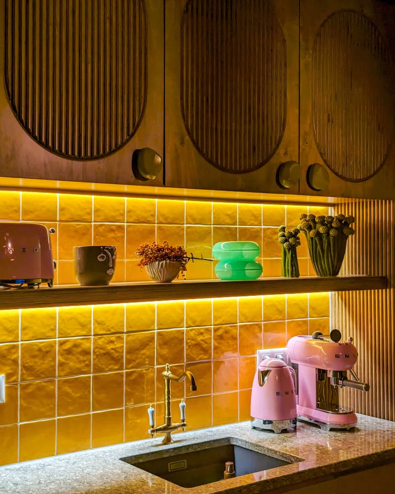 Lights under cabinets on very yellow tile backsplash in newly renovated kitchen.