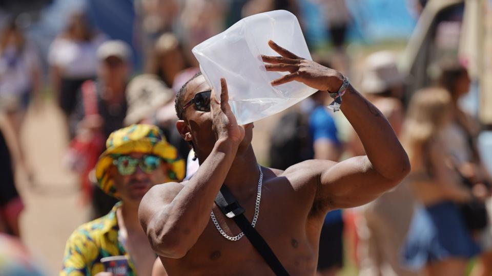 A man walking through the festival site on a hot day is seen drinking from a large plastic water container. 