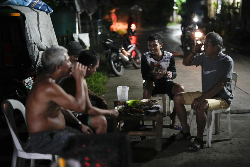 Jeremy Garing drinks with his neighbors outside their house in Tacloban, central Philippines on Wednesday, Oct. 26, 2022. Garing and his family settled three years ago in a new community for victims of Typhoon Haiyan after their village was wiped out in 2013, killing six family members and his daughter. (AP Photo/Aaron Favila)