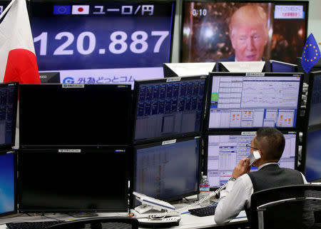 An employee of a foreign exchange trading company works near monitors showing U.S. President-elect Donald Trump (top R), and the Japanese yen's exchange rate against the euro in Tokyo, Japan, January 18, 2017. REUTERS/Toru Hanai