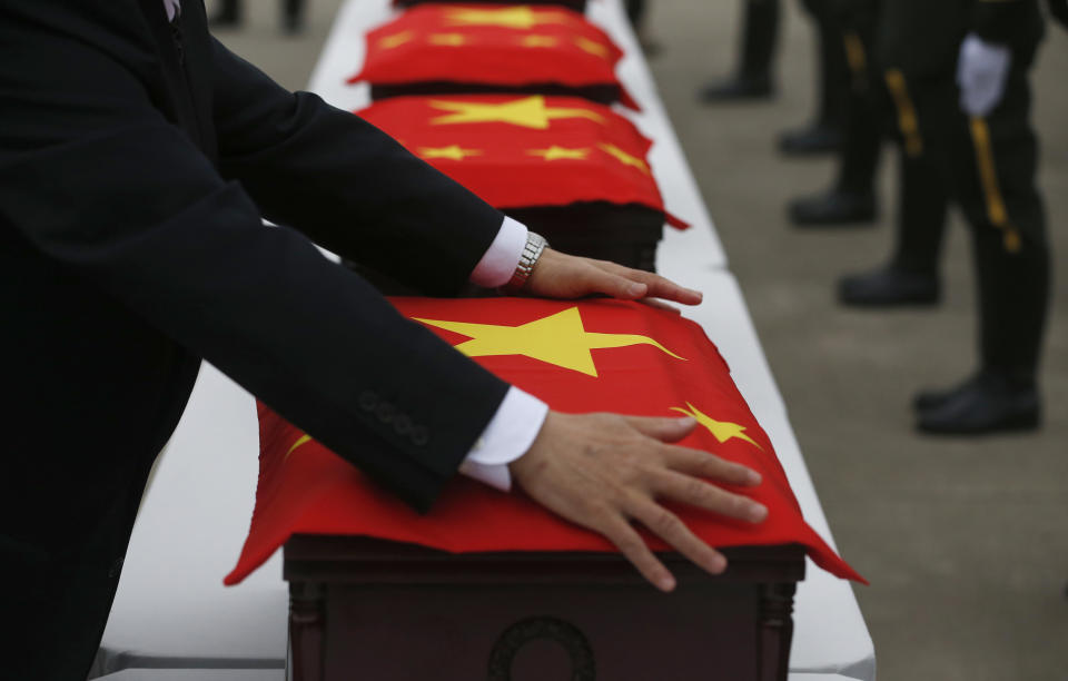 Chinese Ambassador to South Korea Qiu Guohong covers caskets containing the remains of Chinese soldiers with a Chinese national flag during the handing over ceremony of the remains at the Incheon International Airport in Incheon, South Korea Friday, March 28, 2014. The remains of more than 400 Chinese soldiers killed during the 1950-53 Korean War were transferred from the temporary columbarium in South Korea to the airport to return home for permanent burial. (AP Photo/Kim Hong-ji, Pool)