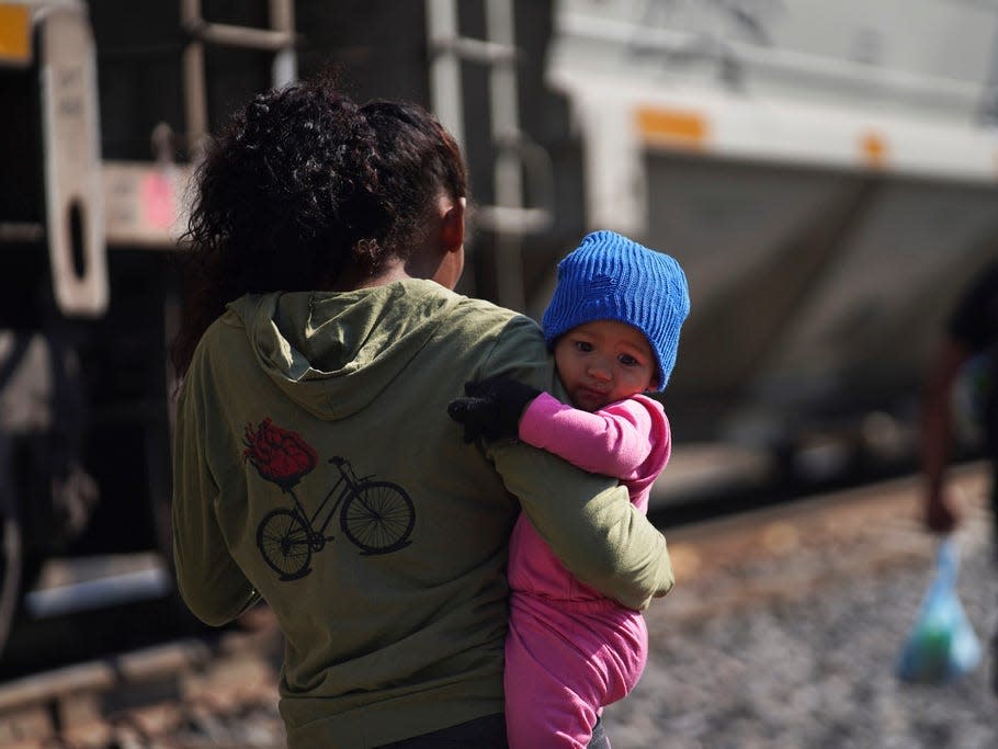 A migrant woman, holding a baby, walks along the train tracks