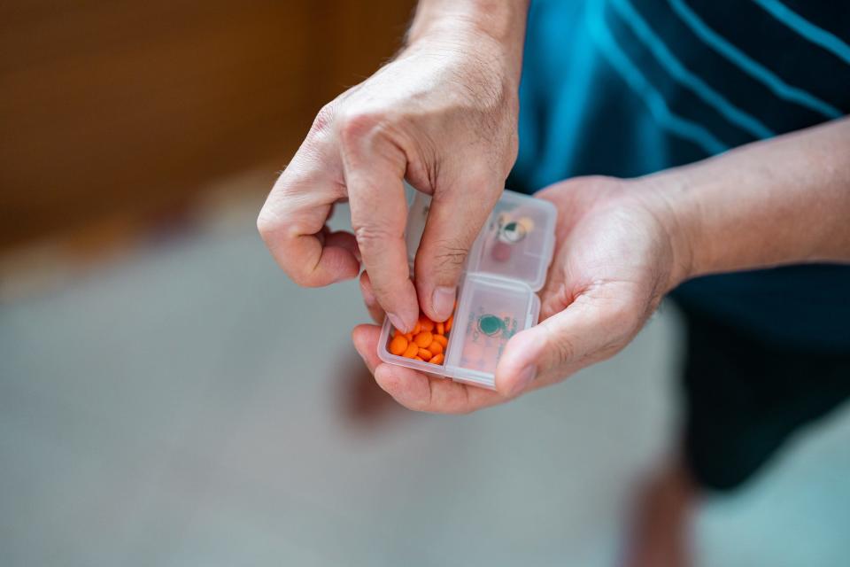 A person holding a tiny pill container filled with orange tablets.