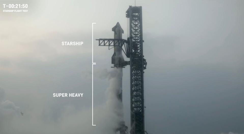 starship super heavy rocket long black on foggy launch pad next to black launch tower