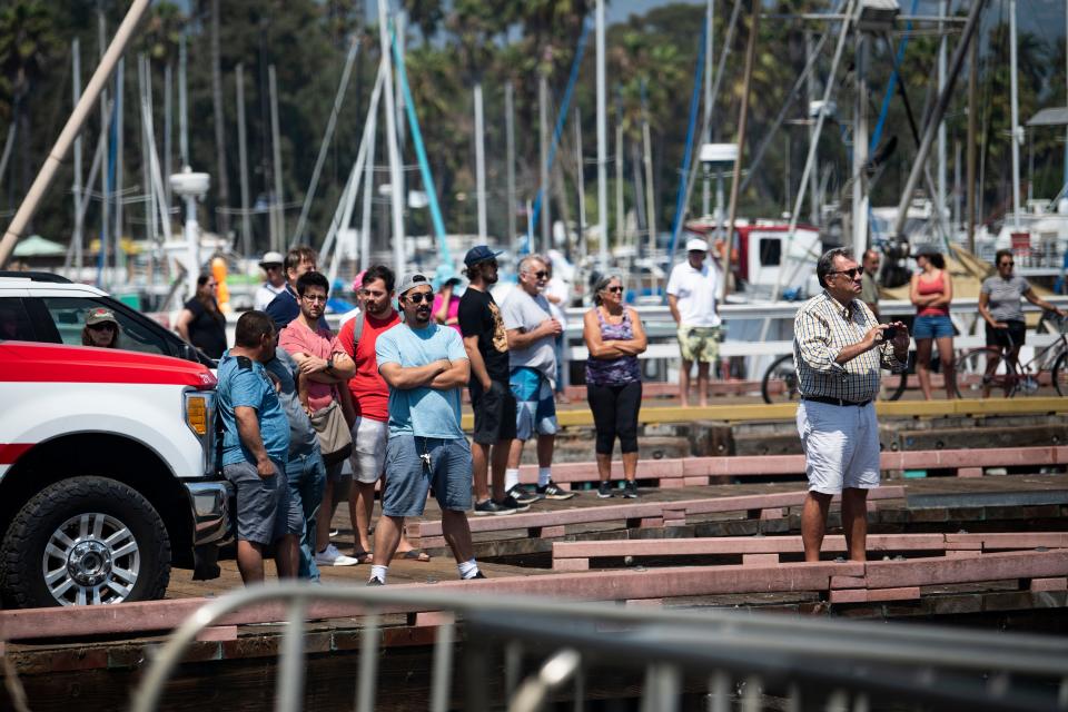 Bystanders watch and record video as United States Coast Guard members transfer a body at the Santa Barbara Harbor on Sept. 2, 2019.