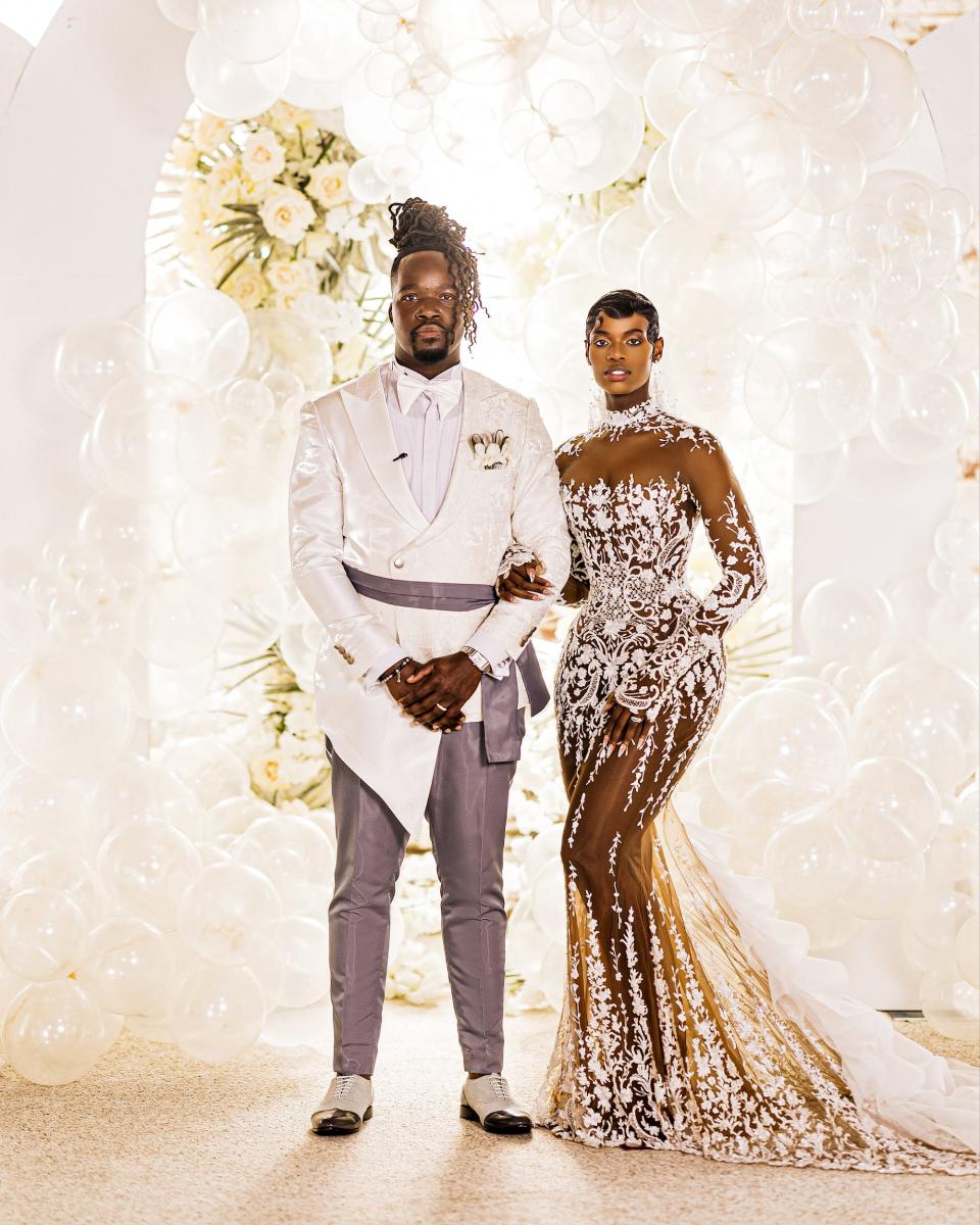 A bride and groom pose in front of a balloon arch.