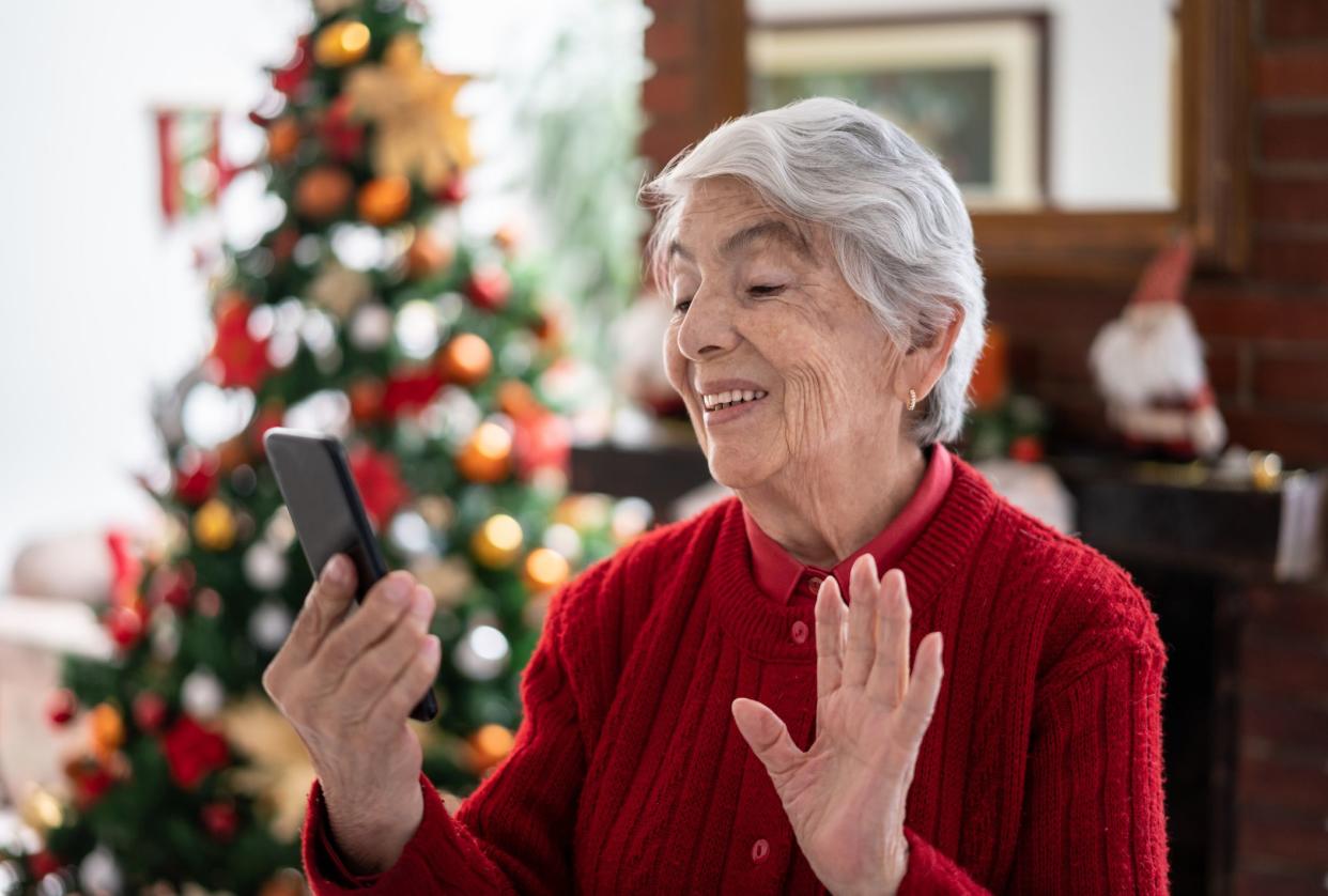 Loving senior woman at home on a video call using a smartphone during christmas season waving hello very happy and smiling - Lifestyles
