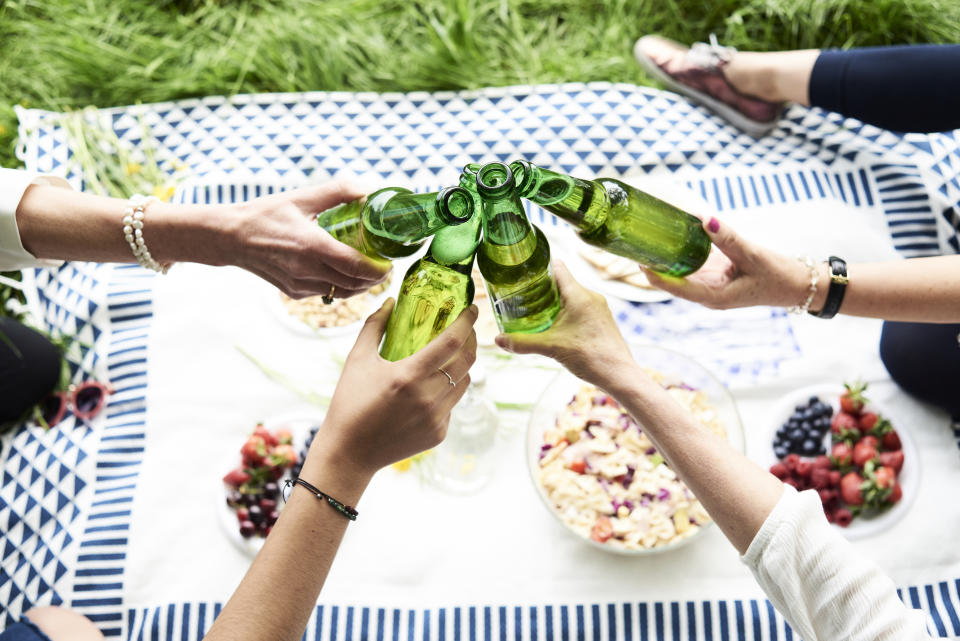 Freunde auf einer picknickdecke stoßen mit grünen Glasflaschen an, Essen auf Picknickdecke