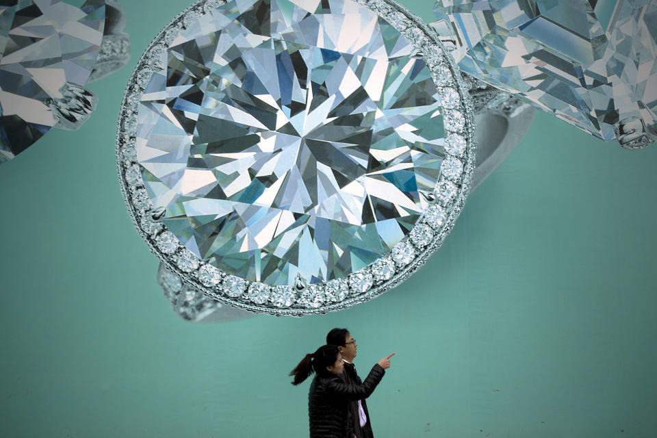 FILE - In this Nov. 9, 2013 file photo, a Chinese couple walk past a billboard depicting diamonds at a commercial street in Beijing, China. Growth has marched steadily downward over the past two years as Beijing clamped down on a spending boom that analysts worry has pushed debt to dangerous levels. (AP Photo/Andy Wong, File)