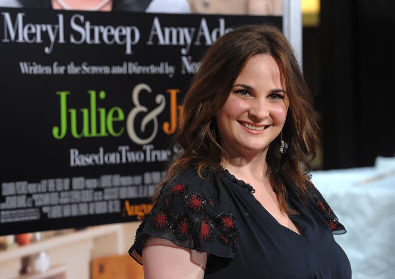 A woman with long brown hair wearing a black dress and smiling