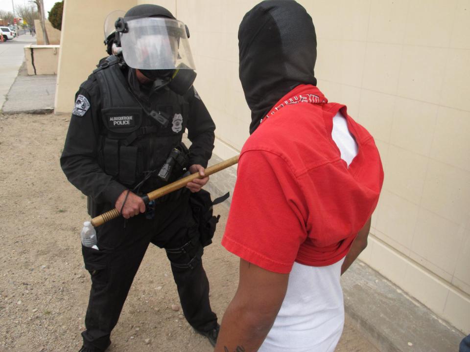 A protester faces off with an Albuquerque officer during a rally against recent police shootings in Albuquerque, N.M. on Sunday March 30, 2014. Hundreds of protesters marched past riot police in Albuquerque on Sunday, days after a YouTube video emerged threatening retaliation for a recent deadly police shooting. The video, which bore the logo of the computer hacking collective Anonymous, warned of a cyberattack on city websites and called for the protest march. (AP Photo/Russell Contreras)