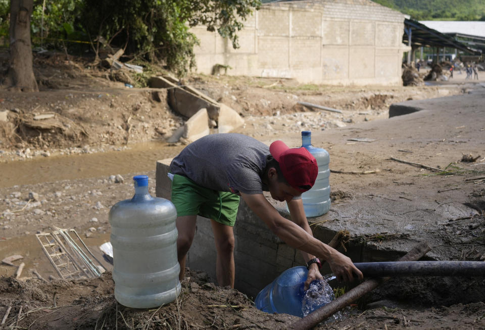 A man fills containers with potable water from a broken pipe connected to a well, to distribute to the community after a landslide ripped through Las Tejerias, Venezuela, Monday, Oct. 10, 2022. The fatal landslide was fueled by days of torrential rain and floods that swept through this town in central Venezuela. (AP Photo/Matias Delacroix)