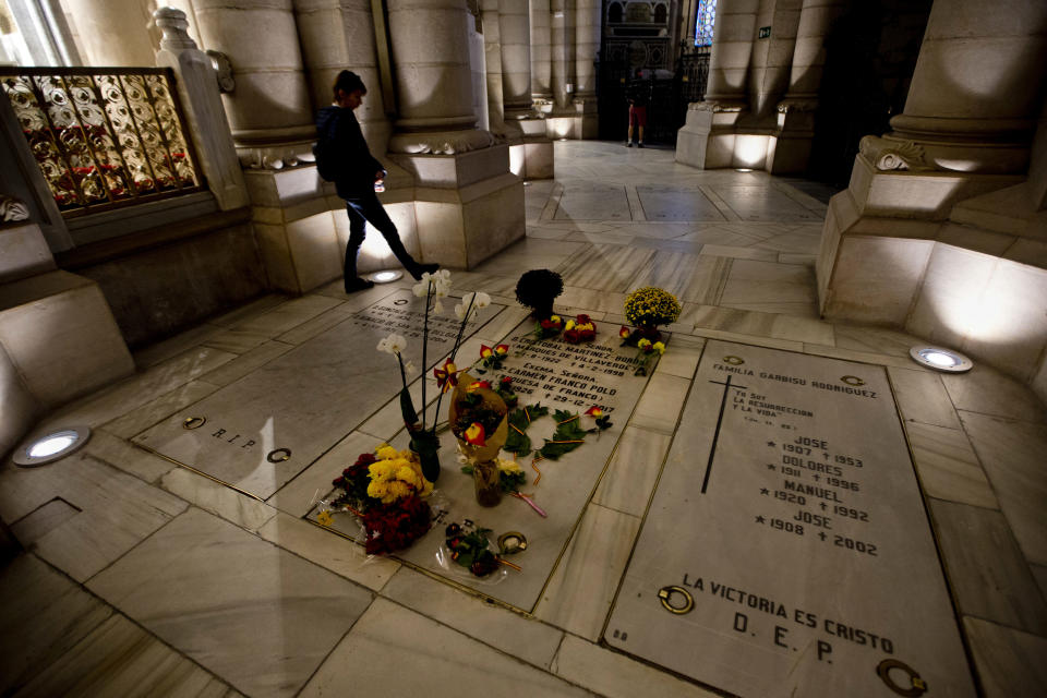 A person walks by the Franco family burial space adorned with flowers in the Almudena Crypt, a cavernous late-19th century Catholic temple under Madrid's Almudena cathedral, in central Madrid, Spain, Thursday Oct. 25, 2018.Hundreds of protesters in Madrid are urging government and Catholic church authorities to prevent the remains of the country’s 20th century dictator from ending in the city’s cathedral. Spain’s center-left government has promised to exhume this year Gen. Francisco Franco from a glorifying mausoleum, but the late dictator’s heirs have defied the plans by proposing for his remains to be relocated to a family crypt under the cathedral. (AP Photo/Paul White)