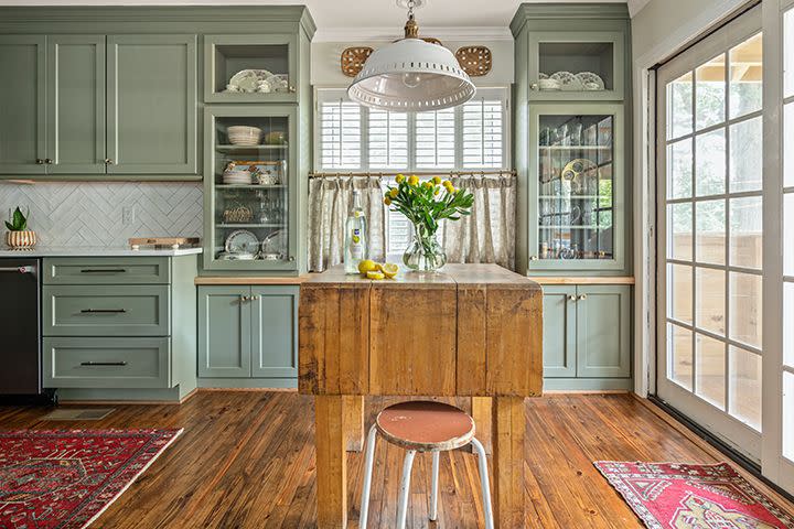 green kitchen cabinets with glass fronts and an antique butcher block island