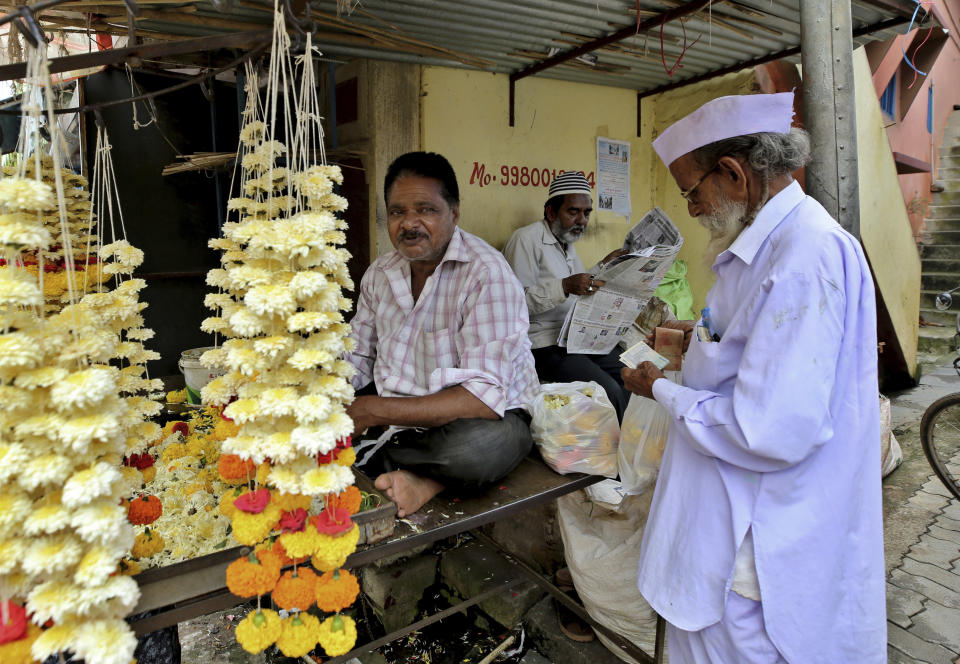 A Muslim man, center, reads a newspaper as a Hindu man buys flowers from a vendor at a market in Belagavi, India, Oct. 7, 2021. Couples in major cities like Delhi and Mumbai are increasingly likely to eschew traditional norms such as arranged marriages and choose life partners irrespective of religion. Some liberal activists, most of them Hindus, have formed social and legal aid groups for interfaith couples and celebrate their stories on social media. But in Belagavi, a relatively small city, such resources and support are lacking. (AP Photo/Aijaz Rahi)