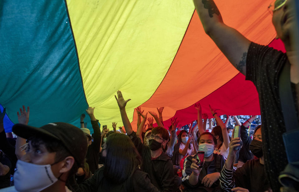 Pro-democracy activities display a rainbow flag during a protest at Democracy Monument in Bangkok, Thailand, Sunday, Aug, 16, 2020. Protesters have stepped up pressure on the government demanding to dissolve the parliament, hold new elections, amend the constitution and end intimidation of the government's opponents. (AP Photo/Gemunu Amarasinghe)