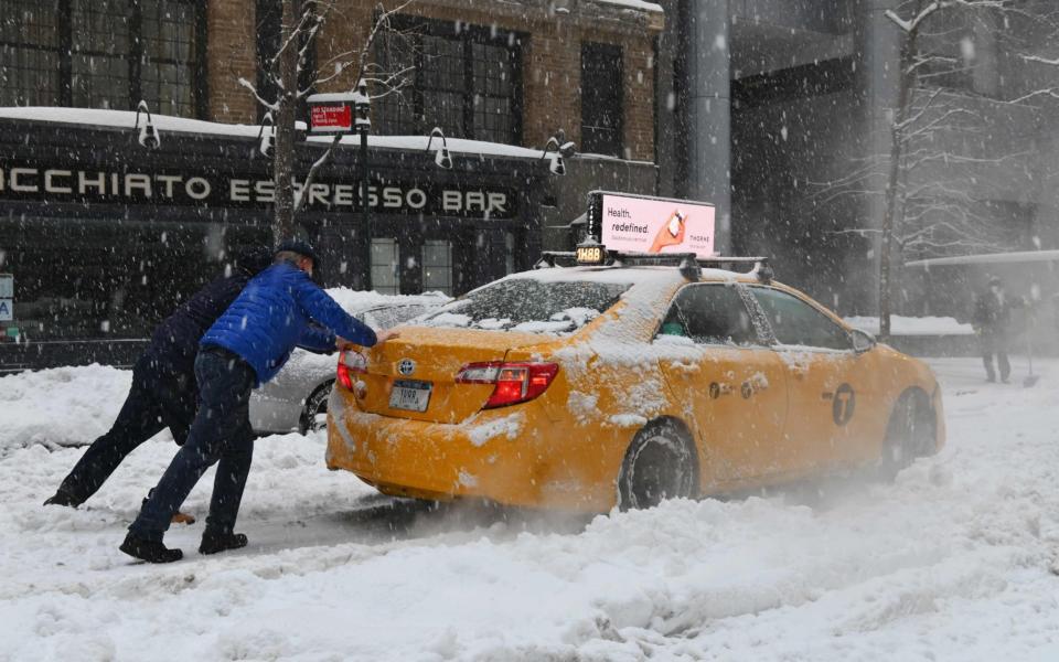 People push a taxi cab stuck on snow covered street  - Angela Weiss / AFP