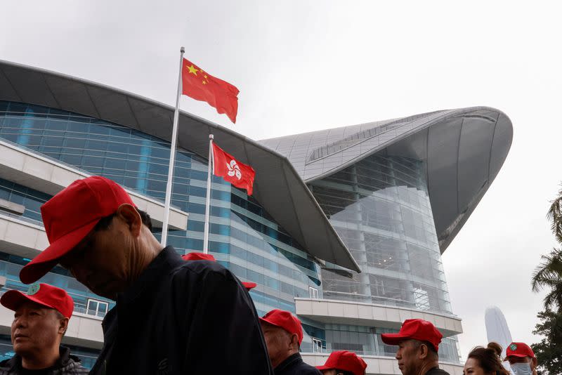 Chinese tourists walk in front of the Chinese and Hong Kong flags, outside the Convention and Exhibition Centre, in Hong Kong