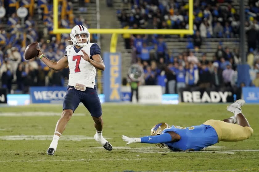 Arizona quarterback Jayden de Laura, left, throws a touchdown pass as UCLA defensive lineman Jacob Sykes reaches for him