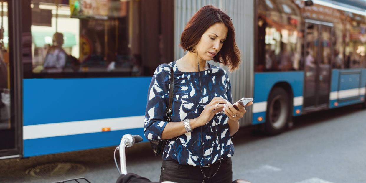 woman on street with bike looking at phone earphones