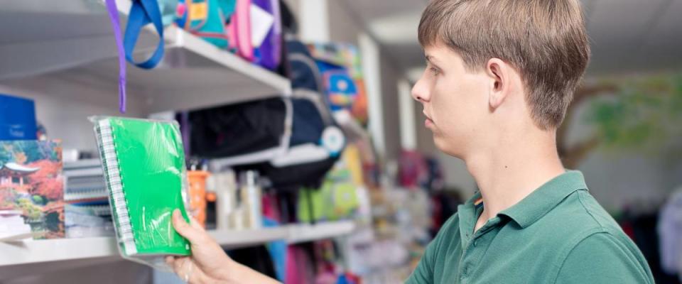 Buying school supplies at the supermarket. The young man buys a notebook in the store