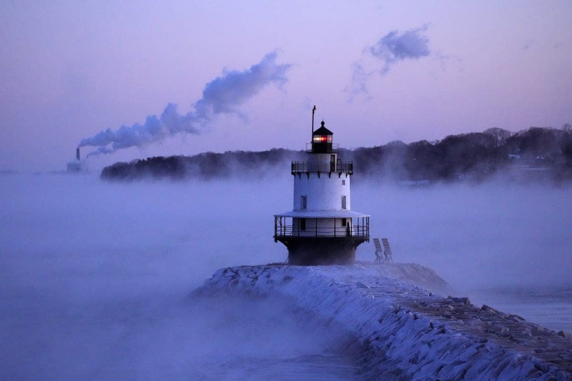 Spring Point Ledge Light is surrounded by arctic sea smoke while emissions from the Wyman Power plant, background, are blown horizontal by the fierce wind, Saturday, Feb. 4, 2023, in South Portland, Maine. The morning temperature was about -10 degrees Fahrenheit. (AP Photo/Robert F. Bukaty)