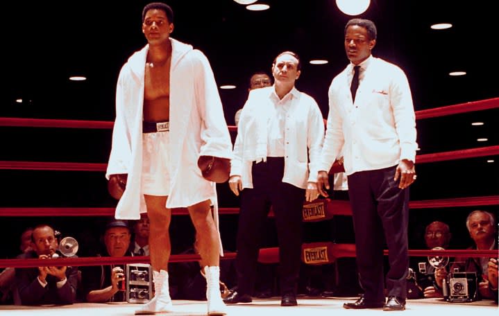 Three men stand in a boxing ring in Ali.