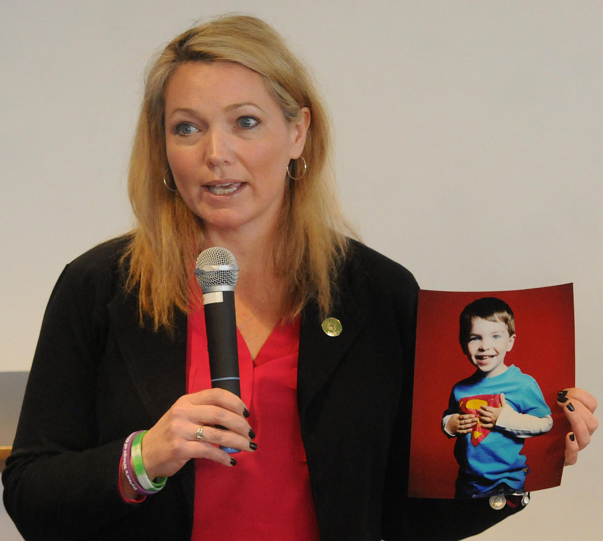 Nicole Hockley speaks into a microphone while holding a photo of her son Dylan, wearing a Superman T-shirt.